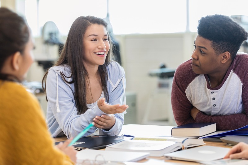 aluna conversa com outros alunos sentados na mesa instruindo como ser lider