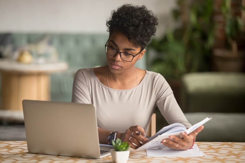 uma estudante na frente de um notebook com caderno na mao enquanto presta vestibular online