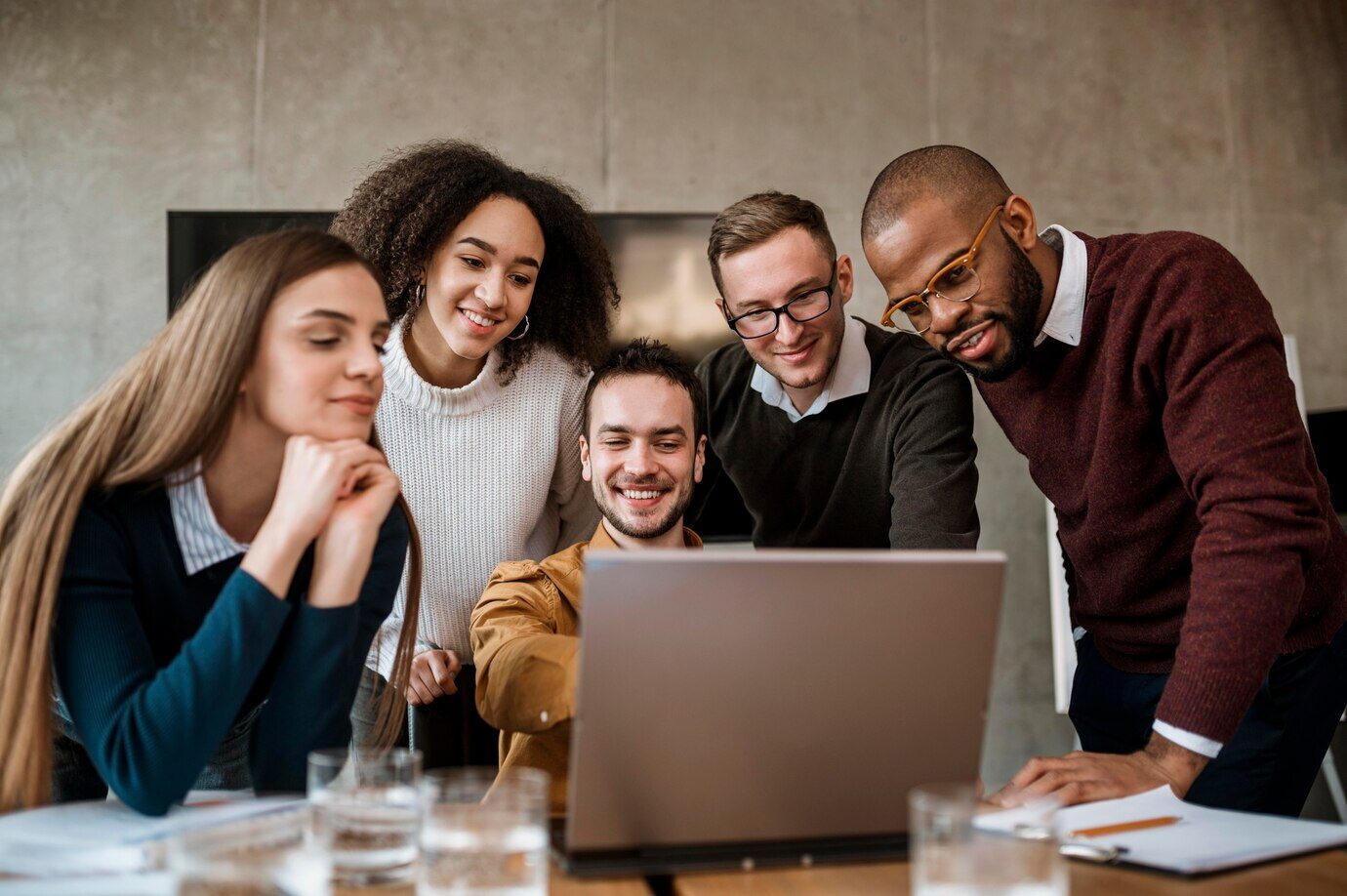homem-sorridente-mostrando-algo-para-seus-colegas-no-laptop-durante-uma-reuniao-de-trabalho