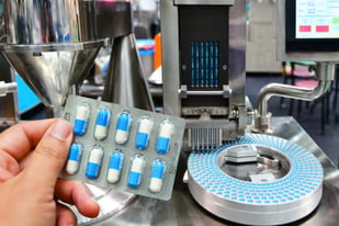 mao-segurando-pilulas-de-remedio-sendo-produzidos-na-industria
