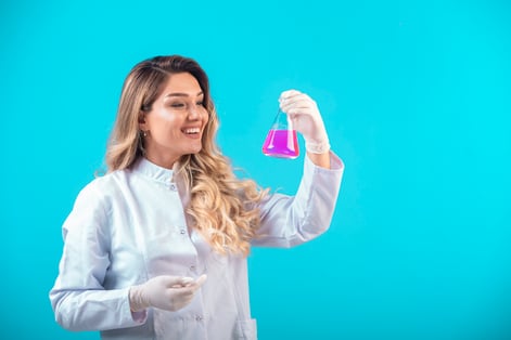 enfermeira de uniforme branco segurando um frasco com liquído rosa 